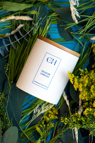 Flat lay photo of herbal scented candle on bed of grass, greenery, and flowers