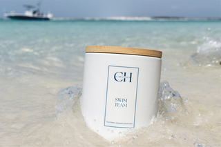 Candle with a wooden lid on a sandy beach with ocean and boat in the background