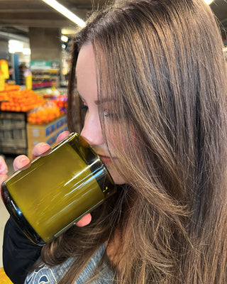 a woman with long brown hair in a grocery store smelling a candle in a green class container